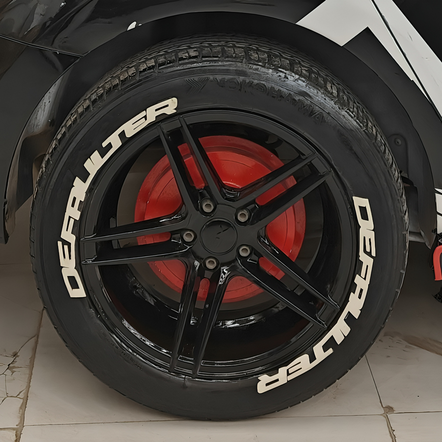 Black alloy wheel with Defaulter tyre sticker on a sleek car showcasing stylish detailing