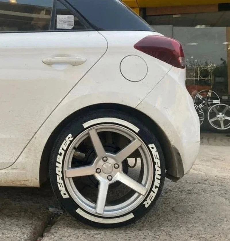 White car with Motorik DEFAULTER tyre stickers on stylish alloy wheels in a garage setting