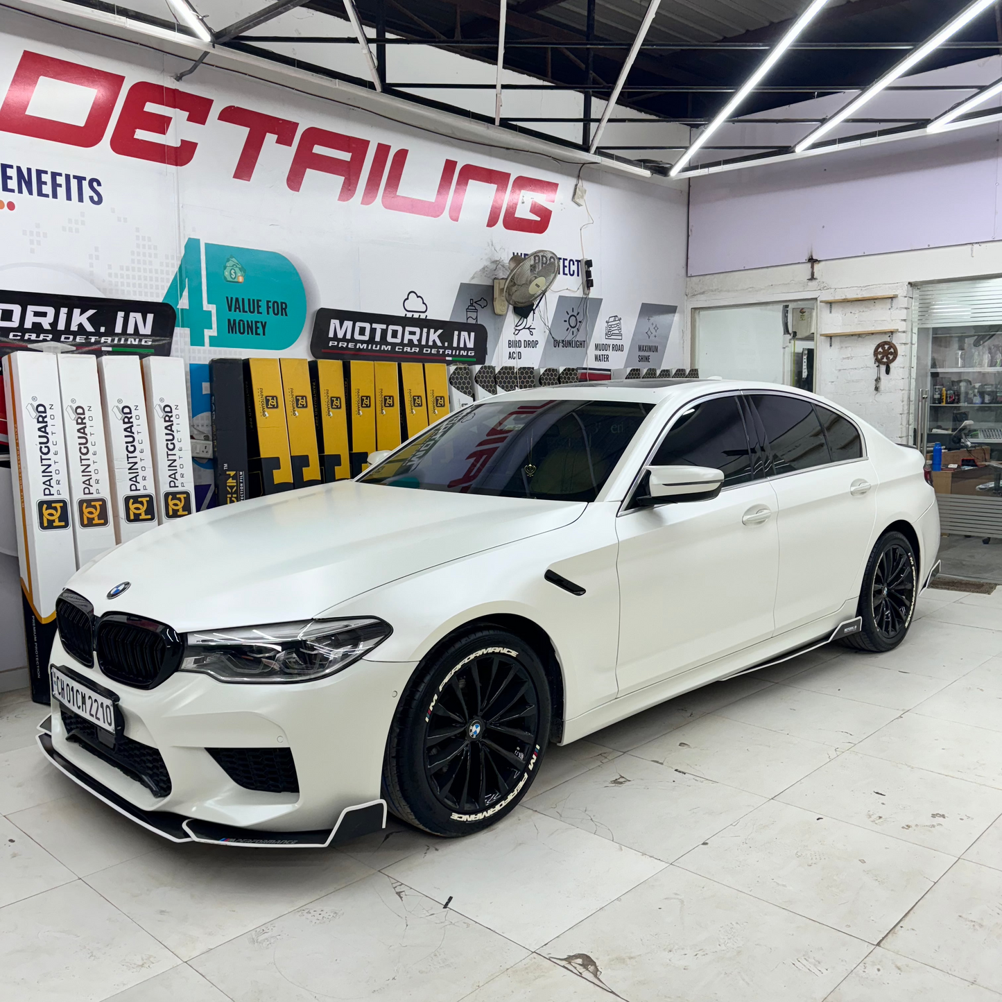 White BMW M5 with M Performance tire stickers, showcased in a modern detailing workshop