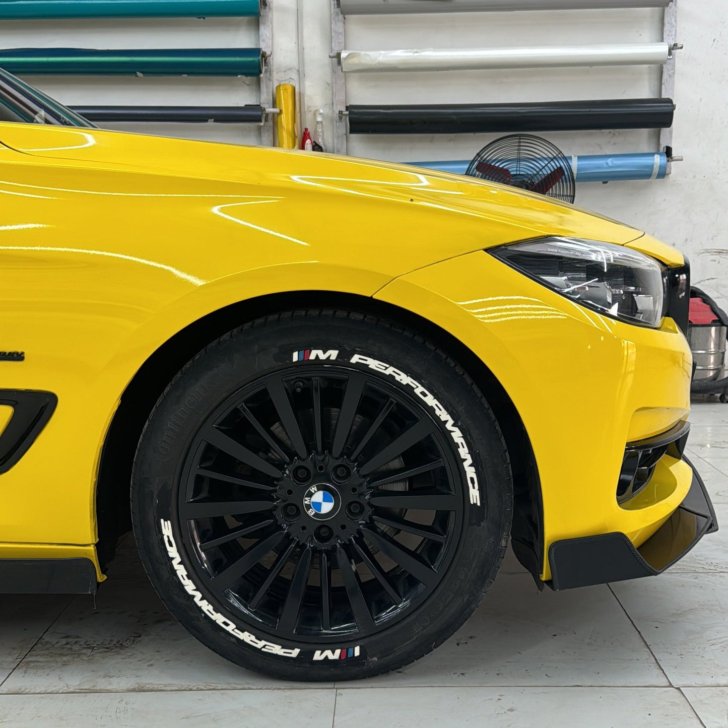 M Performance tire stickers on a black wheel of a yellow BMW car for enhanced sporty appearance