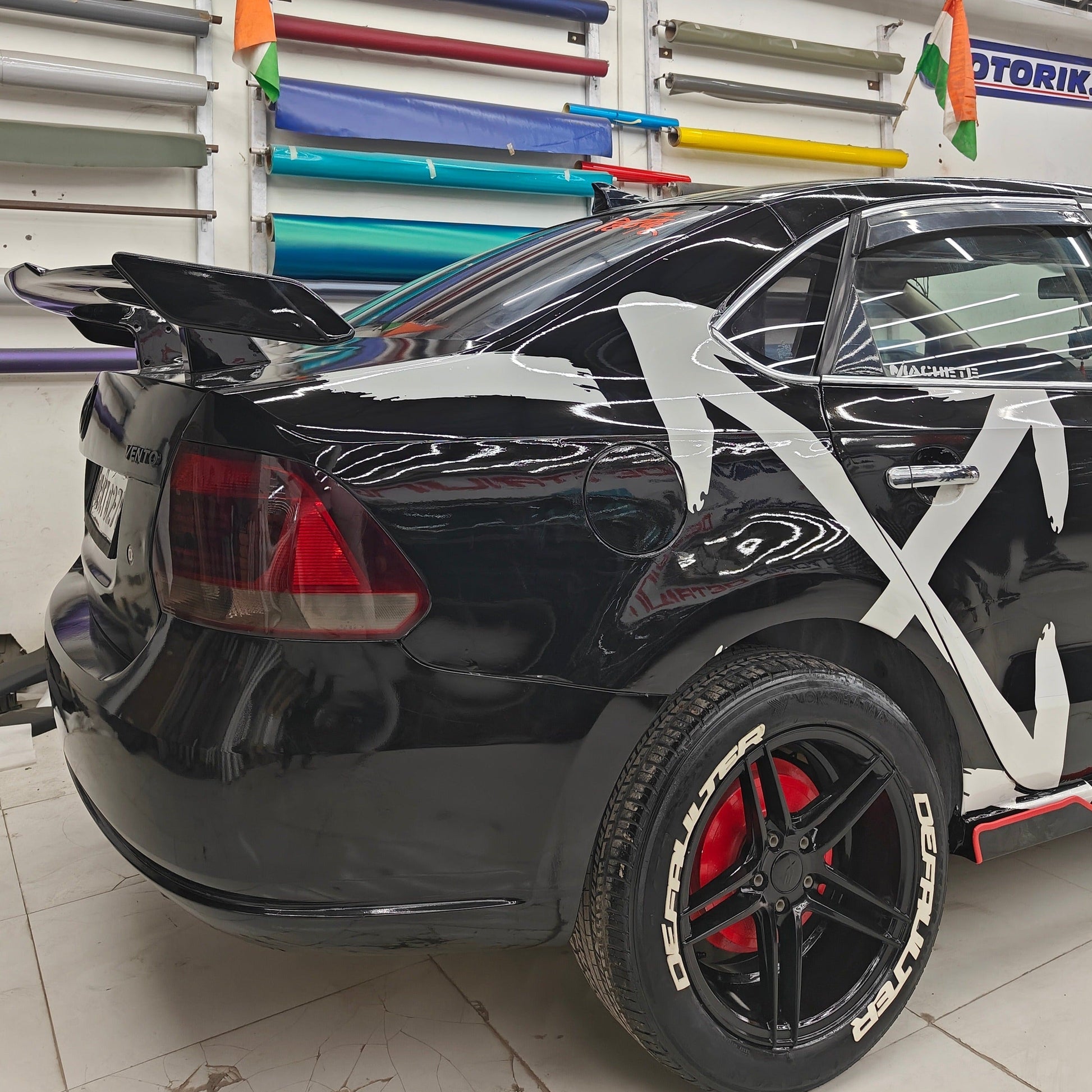 Close-up of a black car featuring ARROW X car graphics and distinctive red and black wheels